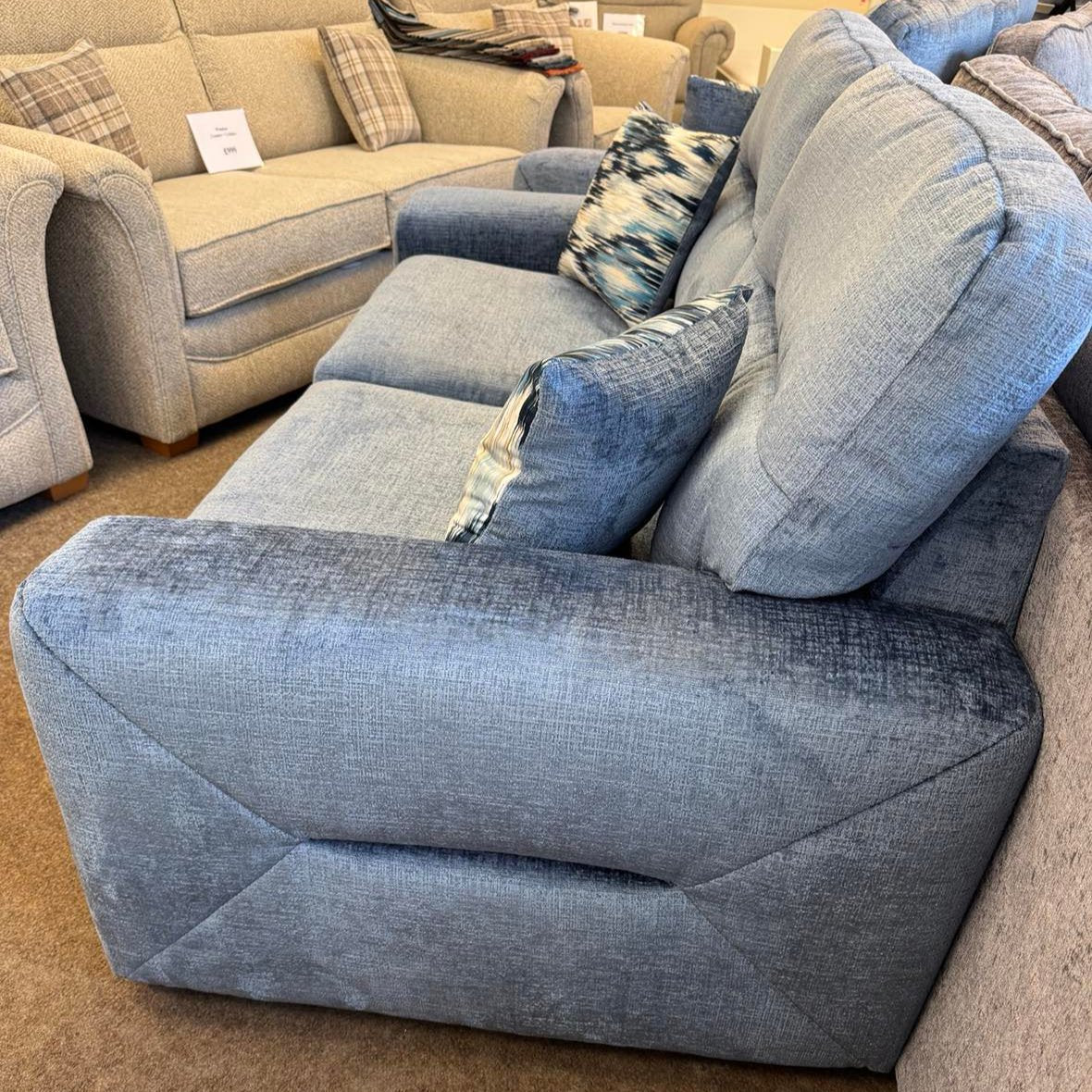 side angle of the mel 2 seater sofa in denim blue. beautifully hand craftmanship on the sides creating a modern sofa for all the family to enjoy. Available to order at Quality Plus Furniture in Lancaster, Lancashire also delivering to Morecambe and Carnforth